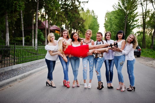 Crazy company of bridesmaids holding bride in red dress in the park at bachelorette party. photo