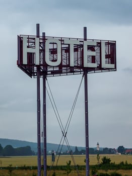 Vertical shot of a Hotel sign on a pole against a blue cloudy sky during the daytime photo