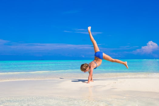 Adorable little girl having fun making cartwheel on tropical white sandy beach photo