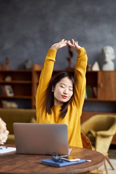 Asian woman working on laptop at home or in cafe stretching tiredly photo