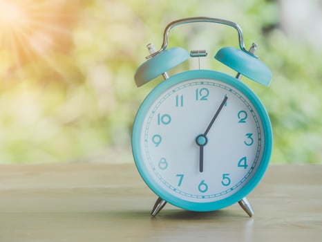 Retro alarm clock 6 o'clock AM or PM with morning sun with flare light   blur green background on wooden table. photo