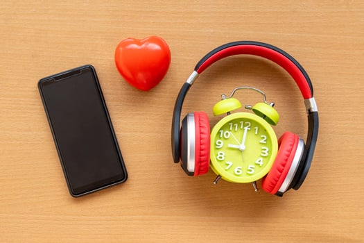Headphones and alarm clock and smartphone and red heart on wooden desk. Musical concept photo
