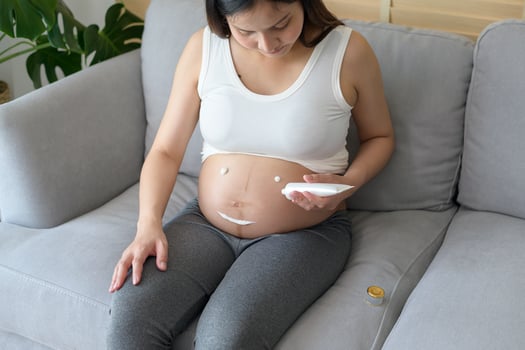 Young pregnant woman applying moisturizing cream on tummy, healthcare and pregnancy care photo