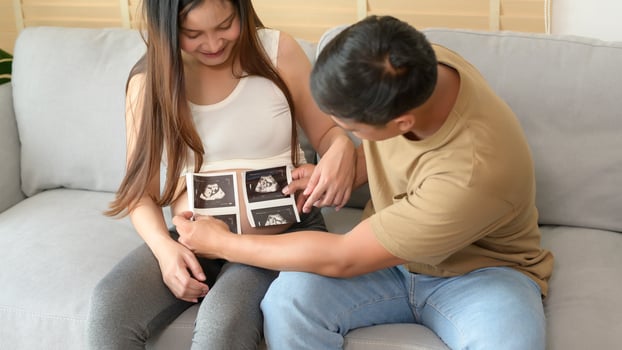 Young pregnant woman with husband holding ultrasound photo of newborn baby, maternity and family concept