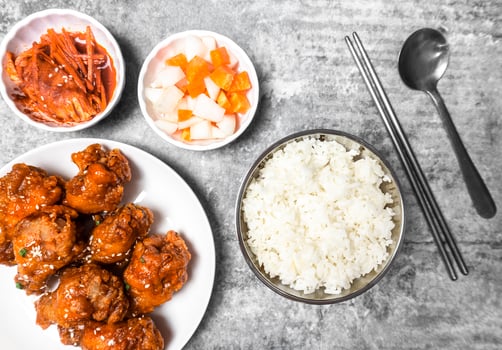 Topview yangnyeom tongdak Korean spicy deep-fried chicken topped white sesame with kimchi and pickled radish side dishes and rice on the gray concrete table, popular street food in Korea. photo