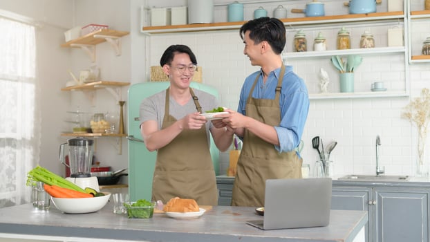 Young smiling gay couple cooking together in the kitchen at home, LGBTQ and diversity concept. photo