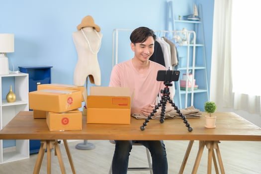 An Asian man is showing clothes in front of smartphone  live streaming at his shop. Technology online business concept. photo