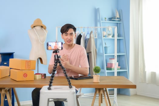 An Asian man is showing clothes in front of smartphone  live streaming at his shop. Technology online business concept. photo