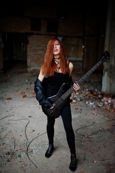 Red haired punk girl wear on black with bass guitar at abadoned place. Portrait of gothic woman musician. photo