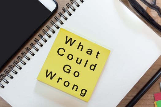 Text on yellow note with notepad on wooden desk - What could go wrong photo