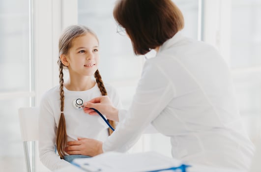 Caring female pediatrician listens childs lungs or heart with phonendoscope. Little girl comes on examination in private clinic, has every year doctor visit, explains symptoms of her disease photo
