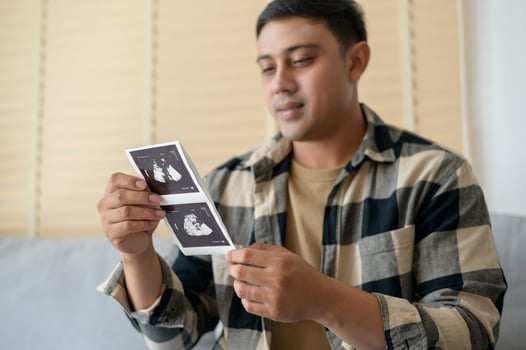Young father holding ultrasound photo of newborn baby, maternity and family concept
