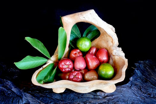 Citrus fruits and guava with leaves in wooden containers, black background photo