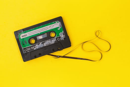 old retro cassette tape with grunge label surrounded by pulled tape pile on yellow background flat lay photo