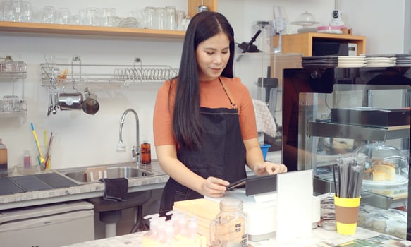 Young woman who is coffee shop business owner wearing an apron standing by a point of sale terminal while working in modern cafe. photo