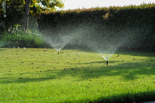 Selective focus on the sprinkle watering around the grass field with blurred background of outdoor garden photo
