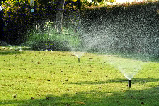 Selective focus on the sprinkle watering around the grass field with blurred background of outdoor garden photo