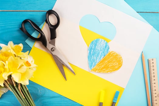 heart cut out of paper and painted in blue and yellow colors and yellow spring flowers on wooding back. Creativity photo