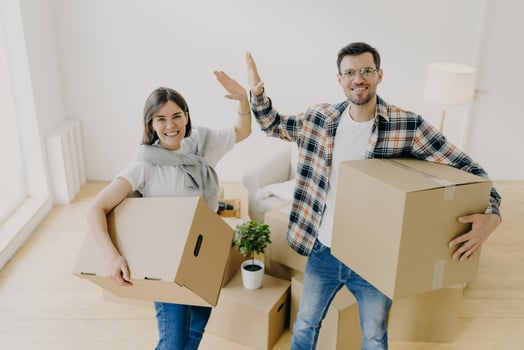 Photo of cheerful young woman and man give high five, smile pleasantly at camera, dressed in casual clothes, start new life, stand in spacious light bedroom. People, repairing and moving concept