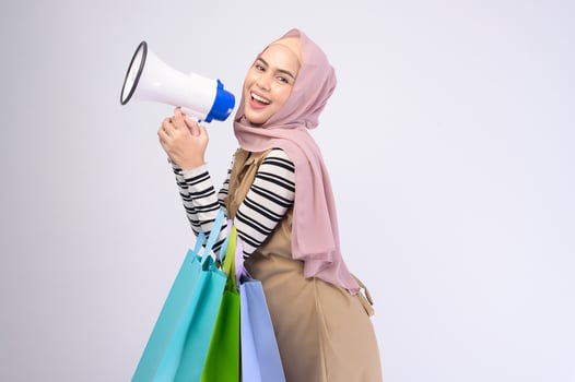 Young beautiful muslim woman in suit holding colorful shopping bags over white background studio photo