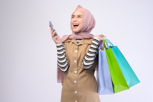 Young beautiful muslim woman in suit holding colorful shopping bags over white background studio photo