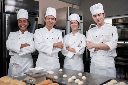 A Group of multiracial professional happy chefs team staff in white cooking uniforms stands in a row, arms crossed with confidence, cheerful smiles with commercial culinary jobs in restaurant kitchen. photo
