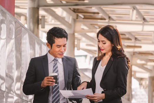 Businessman and business woman walking outside office with paper sheet and coffee cup in hand. photo