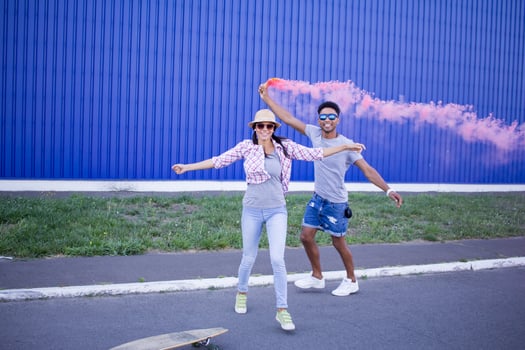 Young couple riding on skateboards with color smoke bomb, boy and girl in casual clothes having good time, pink and blue colors photo