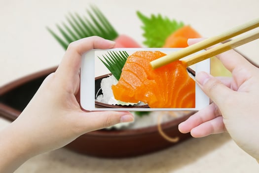 chopsticks hold salmon sashimi in mobile phone photo