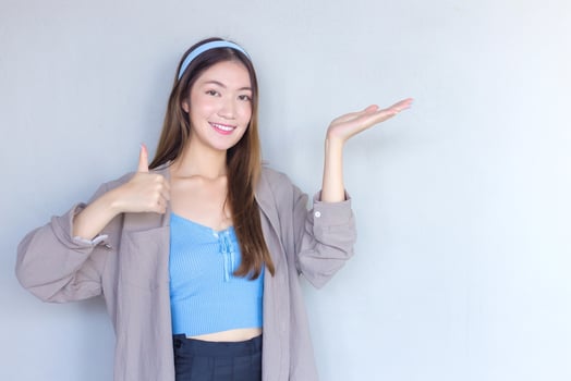 Beautiful young Asian woman is acting thumb up as a good symbol and another hand shows as presenting something on the background. photo
