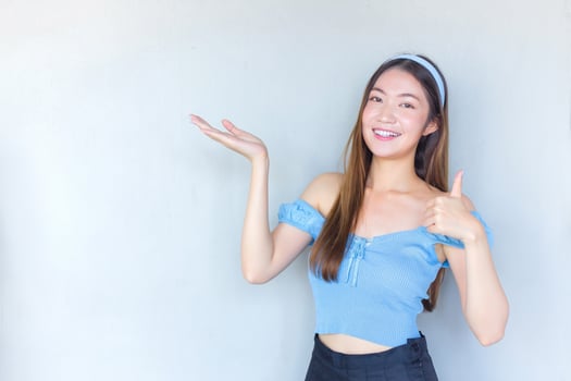 Young beautiful Asian woman in a blue shirt is acting thumb up as a good symbol and another hand shows as presenting something on white the background. photo