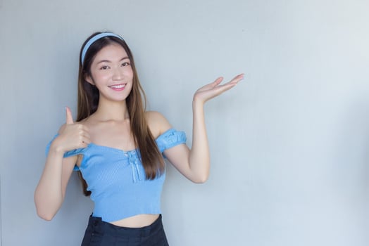 Young beautiful Asian woman in a blue shirt is acting thumb up as a good symbol and another hand shows as presenting something on white the background. photo