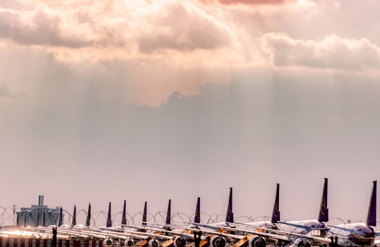 Commercial airplane parked at parking area of the airport after corona virus crisis impact on aviation business. Plane is parked at apron inside the airport fence with sunset sky. Tail of aircraft. photo