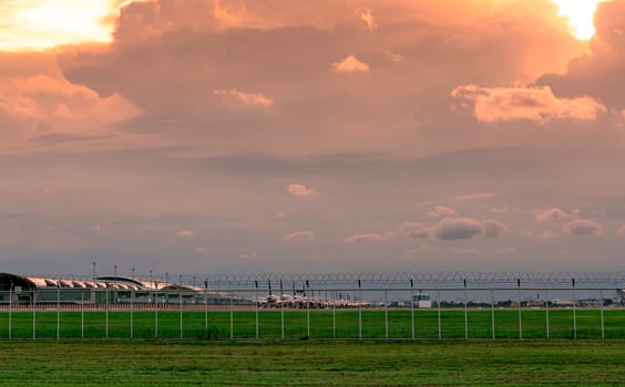 Landscape of green grass field and fence of the airport and beautiful sunset sky. Commercial airplane parked at apron of airport. Coronavirus impacted aviation business. Fence for safety and security. photo