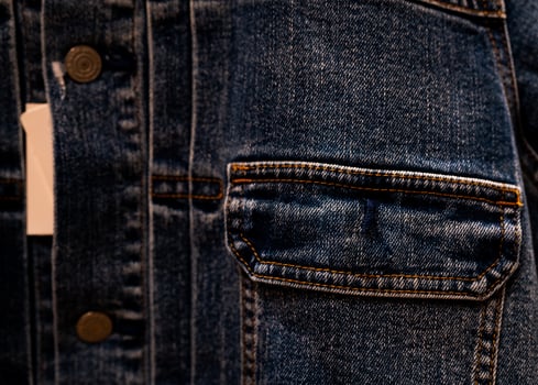 Selective focus on denim jean jacket pocket in clothes shop. Denim jacket pocket texture background. Textile industry. Jeans fashion and shopping concept. Clothing concept. Denim jacket for sale. photo