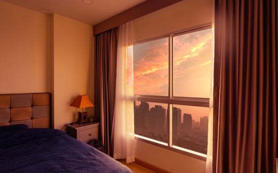 Bedroom in the morning with morning sunlight through glass window with opened curtains. Luxury bed in modern apartment in the city. Bedroom interior. Blue blanket covered bed. View from glass window. photo