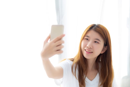 Beautiful portrait young asian woman taking a selfie with smart mobile phone on bedroom in the morning at home, girl is photographing with happy and smile with fun, lifestyle concept. photo