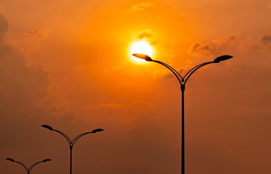 Silhouette street electric pole with beautiful orange and yellow sunset sky and clouds in the evening. Street lamp light. City road lamp post for illumination Power and energy conservation concept. photo