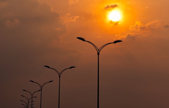 Silhouette street electric pole with beautiful orange and yellow sunset sky and clouds in the evening. Street lamp light. City road lamp post for illumination Power and energy conservation concept. photo