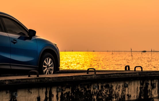 Blue compact SUV car with sport and modern design parked on concrete road by the sea at sunset. Environmentally friendly technology. Electric car technology and business. Hybrid auto and automotive. photo