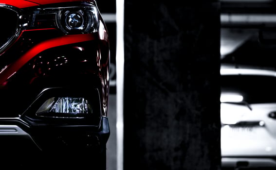 Closeup headlights of red SUV sport car parked near concrete pole at indoor parking lot. Headlamp lights with elegant and luxury design. Automotive industry and hybrid car concept. Underground parking photo