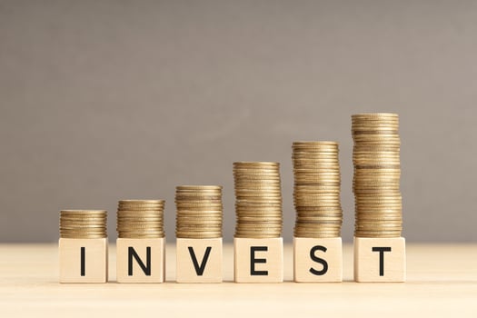 Invest word in wooden blocks with coins stacked in increasing stacks. Investing growing concept. Copy space photo