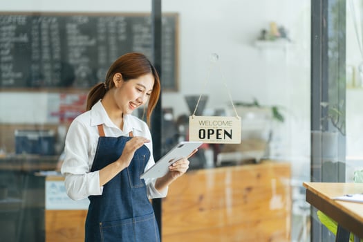 Portrait of happy woman standing at doorway of her store. Cheerful mature waitress waiting for clients at coffee shop. Successful small business owner in casual wearing blue apron standing at entrance photo