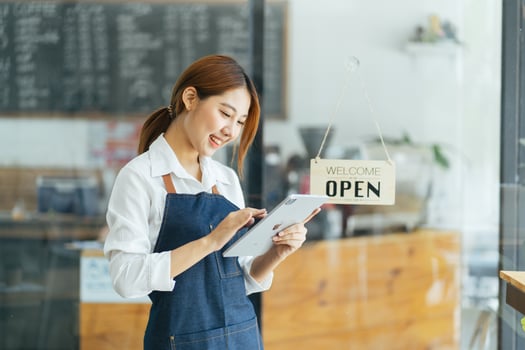 Portrait of happy woman standing at doorway of her store. Cheerful mature waitress waiting for clients at coffee shop. Successful small business owner in casual wearing blue apron standing at entrance photo
