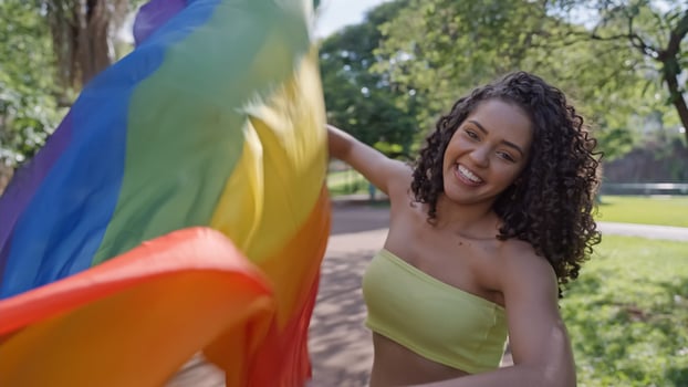 Young curly hair woman covering with lgbt pride flag. Keeping fist up, covering LGBT flag photo
