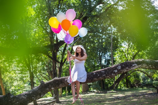 Young teen girl sitting on tree and holding balloons in hand photo