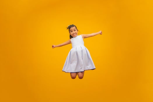 Beautiful asian girl sitting on yellow background. Happy little Asian girl smiling. photo