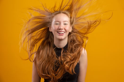 Portrait of beautiful cheerful redhead girl with flying hair smiling laughing looking at camera over yellow background. photo