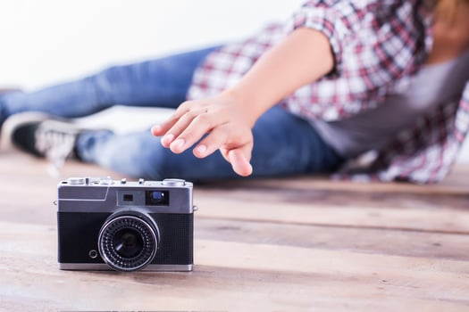 Young hipster photographer woman taking photo and look at camera sitting on wooden floor.
