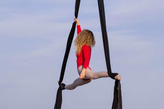 exercises with aerial silk outdoor, sky background. beautiful fit woman training acrobatic in airt. photo